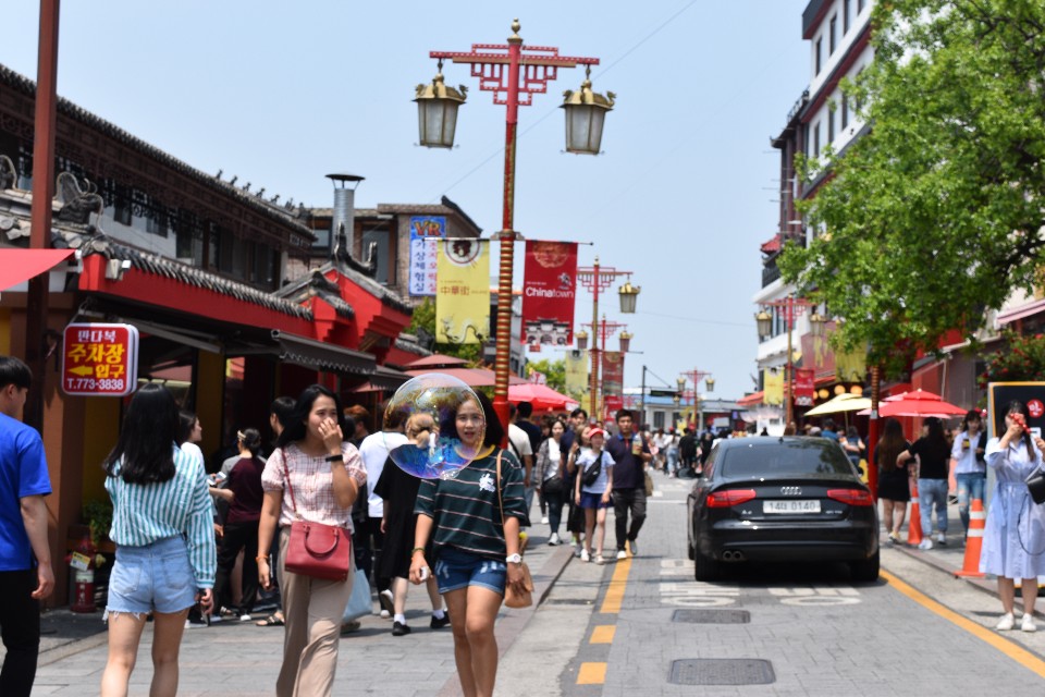 Two people walking down the main street in Incheon chinatown. In the background are people and chinatown restaurants 